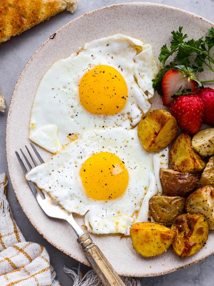 A Sunny Side Up Egg is a perfect way to add protein to a meal, and is a must-have skill in the kitchen! The key is timing and temperature, and following my simple tips you'll whip up the most flavorful and perfectly runny pan-fried egg. A plate of food with eggs, potatoes, and strawberries with a fork.