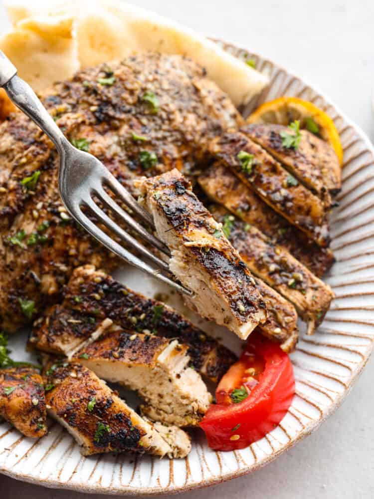 A traditional Middle Eastern spice, this Za'atar seasoning is herby, nutty, and savory. The sesame seeds give a little texture, and make this seasoning perfect for rubs, marinades, or as a topping on your hummus! Chicken with grill marks sliced into strips with a fork holding up a piece of chicken.