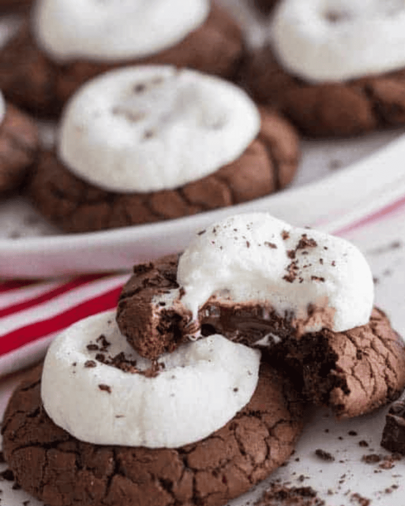 These hot cocoa cookies are the perfect treat for the winter season! These soft and delicious cookies have a marshmallow on top and some ooey, gooey chocolate in the middle. A stack of hot cocoa cookies, the top one with a bite taken out of it.
