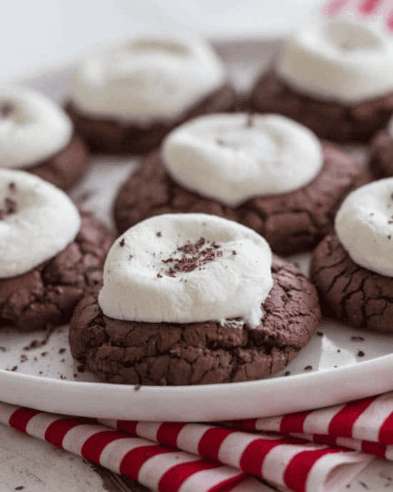 These hot cocoa cookies are the perfect treat for the winter season! These soft and delicious cookies have a marshmallow on top and some ooey, gooey chocolate in the middle. Hot cocoa cookies on a plate, ready to eat.
