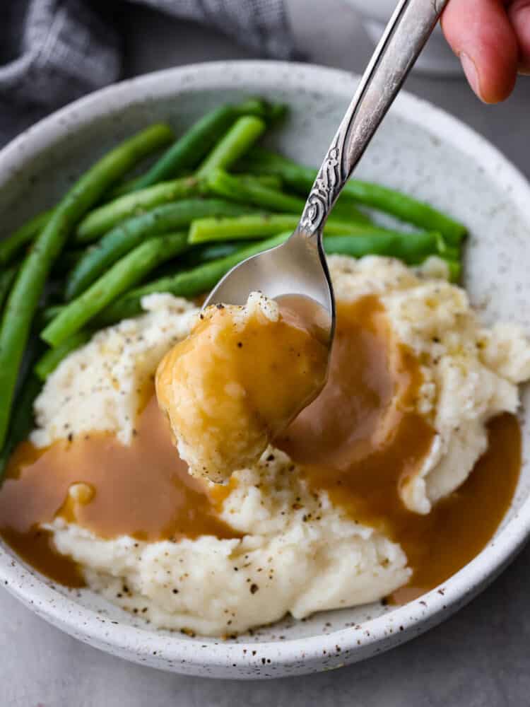This Brown Gravy is quick and easy with no drippings needed! It's made with beef broth and bullion, giving it a rich deep flavor and it's ready in under 10 minutes. It's the perfect addition to any protein or on top of a mountain of mashed potatoes. Brown gravy on top of mashed potatoes with a spoon taking a scoop out of it.