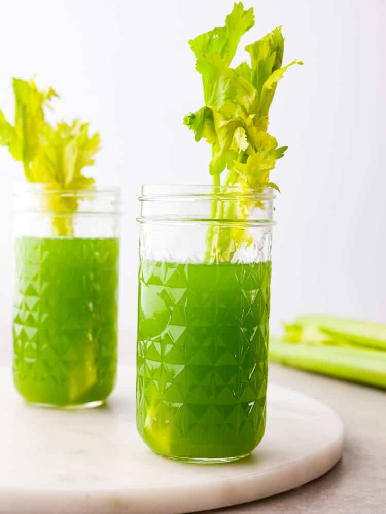 Celery juice is a healthy and refreshing drink full of beneficial nutrients for your body. This healthy juice is simple to make at home and it comes together quickly in a blender. Two glasses of celery juice in mason jars. A leafy celery stalk is styled inside each glass of juice.