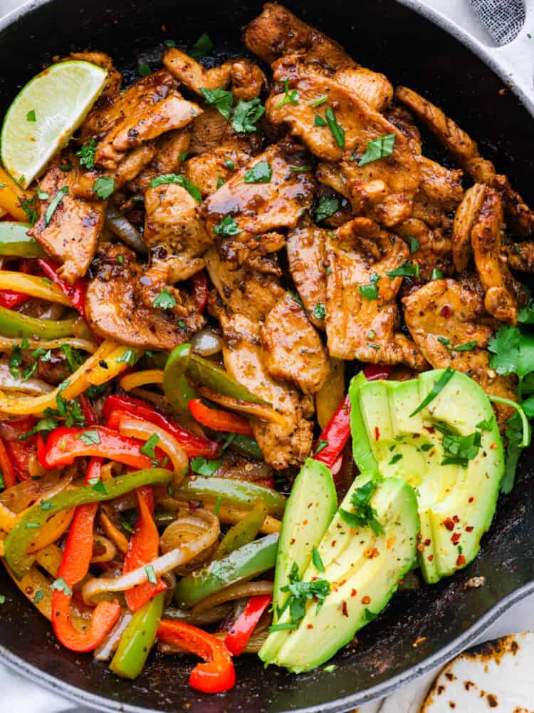 These Chicken Fajitas are served sizzling hot with all of your favorite toppings. This meal needs just one pot and is ready in under 30 minutes. It's flavorful and always a crowd-pleaser! A close up on chicken fajitas with fresh avocado.