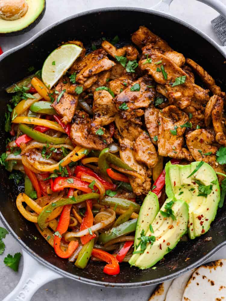 These Chicken Fajitas are served sizzling hot with all of your favorite toppings. This meal needs just one pot and is ready in under 30 minutes. It's flavorful and always a crowd-pleaser! Chicken fajitas in a skillet with fresh lime and cilantro