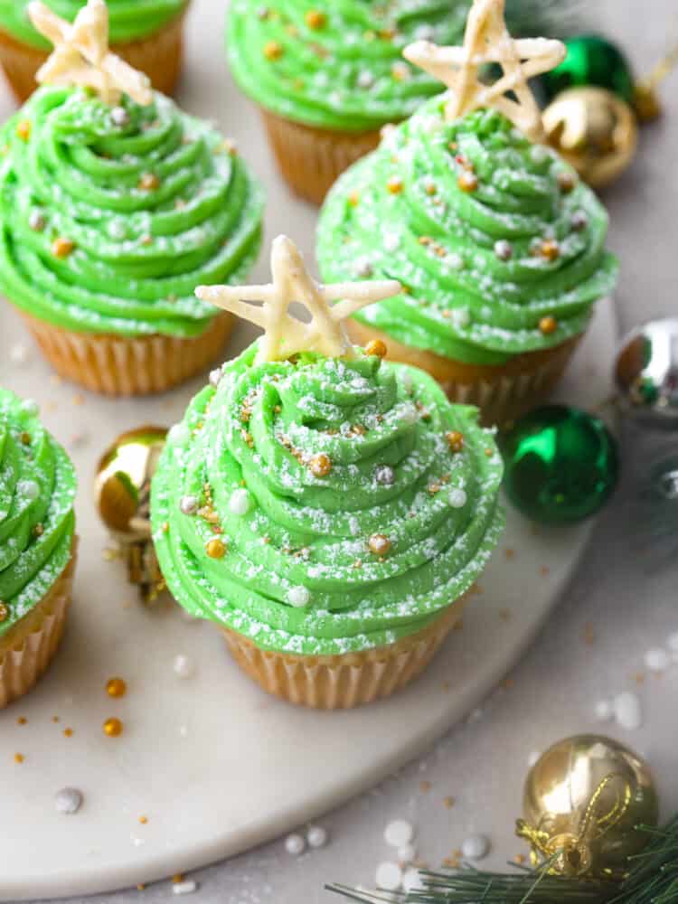 If you're looking for a dessert that is absolutely delicious but also looks great on the holiday dinner table, these Christmas tree cupcakes are it! Moist vanilla cupcakes topped with homemade buttercream frosting that almost look too good to eat! Top-down view of Christmas tree cupcakes, garnished with sprinkles and a pretzel star.