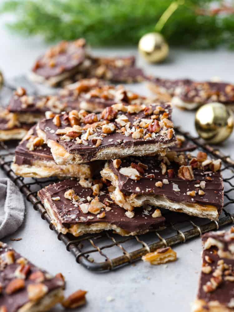 This is the Best Christmas Crack Recipe! It's a saltine cracker layered with toffee and creamy chocolate, then topped with crunchy pecans for the ultimate sweet and salty treat.ย This recipe is so easy, delicious, and addicting! Christmas crack toffee on top of a wire rack with ornaments in the background.