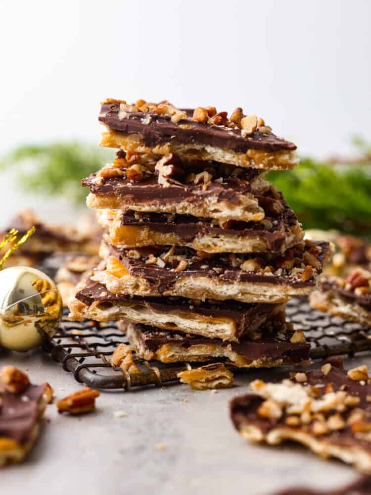 This is the Best Christmas Crack Recipe! It's a saltine cracker layered with toffee and creamy chocolate, then topped with crunchy pecans for the ultimate sweet and salty treat.ย This recipe is so easy, delicious, and addicting! Christmas crack stacked on top of each other with other pieces of Christmas crack around it.