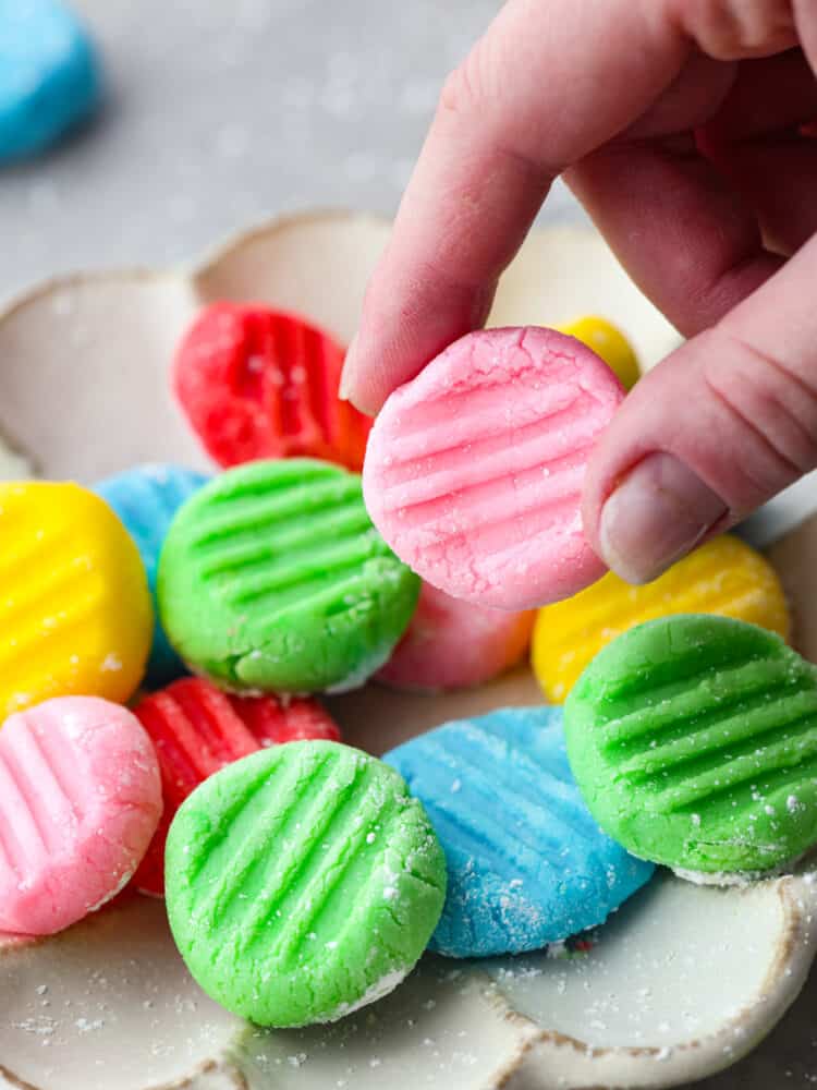 This classic and timeless Cream Cheese Mint is the perfect melt-in-your-mouth candy to make for your next party. They are creamy and sweet with a hint of mint flavor that is so refreshing, you'll want to eat them again and again! A hand holding a pink cream cheese mint above a platter of other mints.