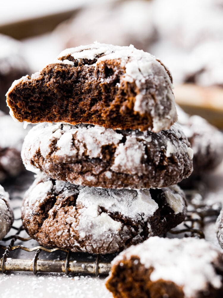 Chocolate crinkle cookies are classic chocolate cookies with a decadent chewy texture. The crinkle top on these rich fudgy cookies have a sweet sugar coating making them everyone's favorite holiday cookie! Close up side view of chocolate crinkle cookies stacked on top of each other with a bite missing from the top cookie