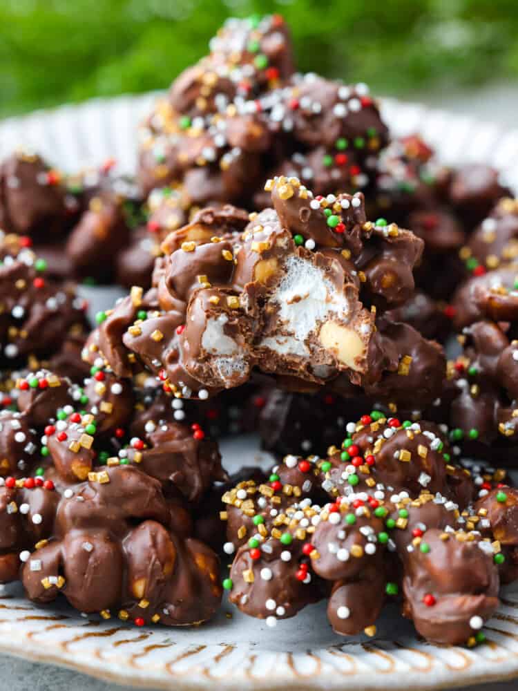 Christmas baking doesn't get much easier than this super simple Crockpot Candy recipe! Made with chocolate, marshmallows, and peanuts, just toss all of the ingredients in your crockpot, mix it together, melt, and scoop and you have one of my family's favorite treats! A plate full of Christmas crockpot candy with a bite taken out of it to show the inside.