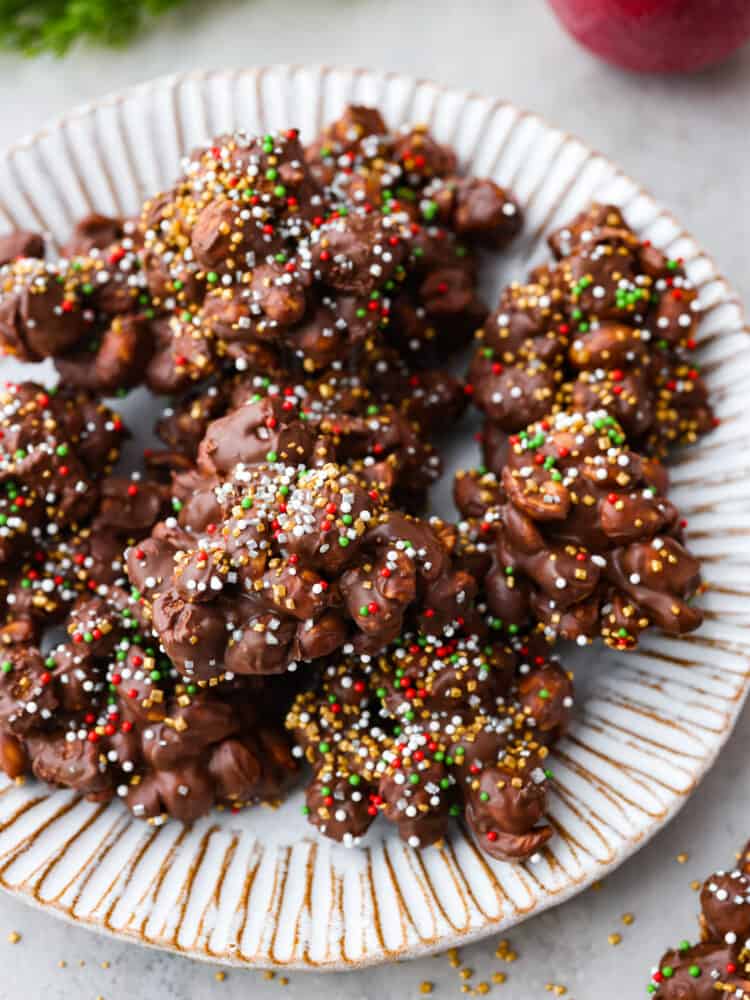 Christmas baking doesn't get much easier than this super simple Crockpot Candy recipe! Made with chocolate, marshmallows, and peanuts, just toss all of the ingredients in your crockpot, mix it together, melt, and scoop and you have one of my family's favorite treats! The crockpot candy on a white plate with sprinkles around the plate.