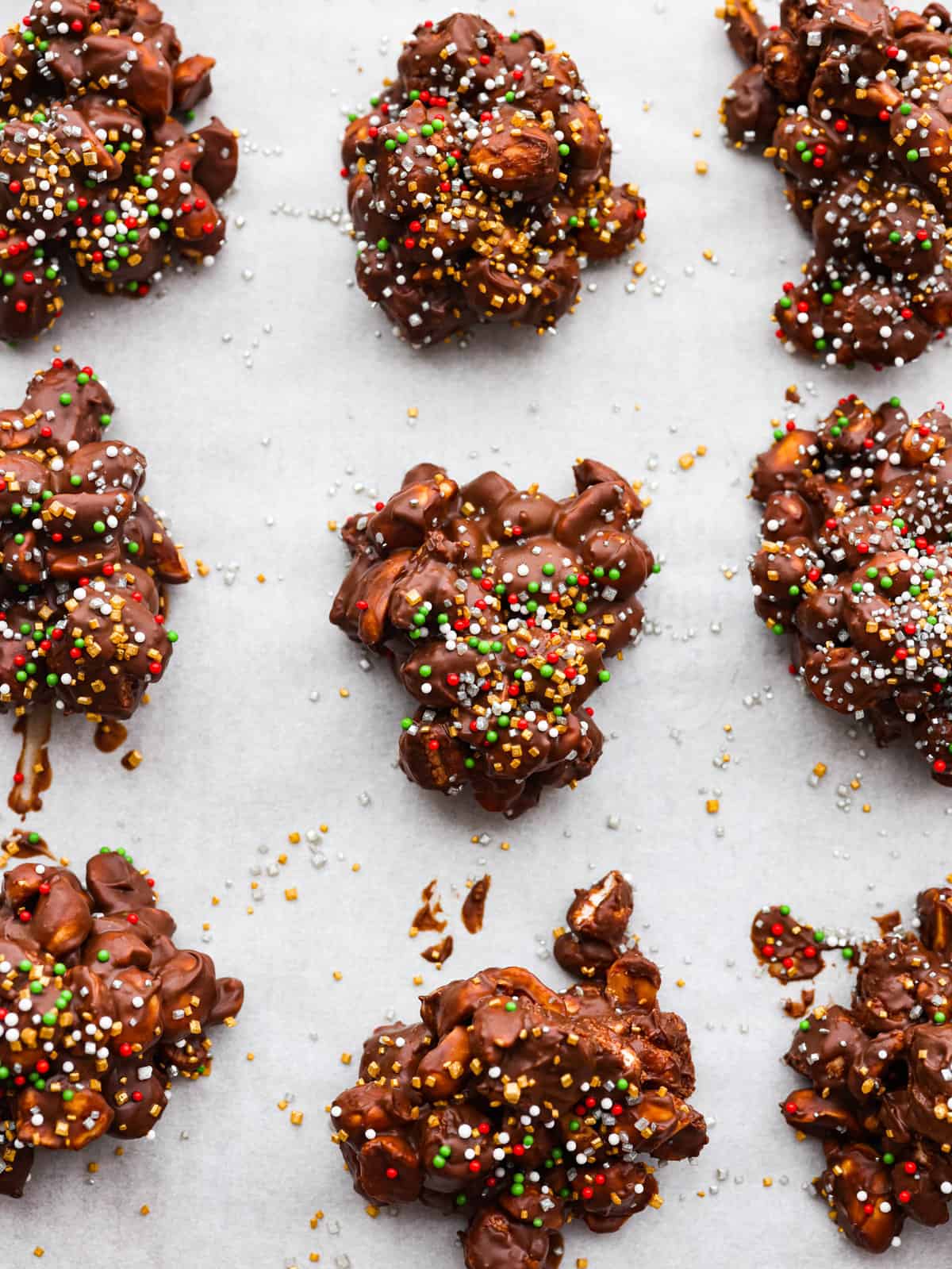 Christmas baking doesn't get much easier than this super simple Crockpot Candy recipe! Made with chocolate, marshmallows, and peanuts, just toss all of the ingredients in your crockpot, mix it together, melt, and scoop and you have one of my family's favorite treats! A close up on the candy nut clusters with sprinkles on top.