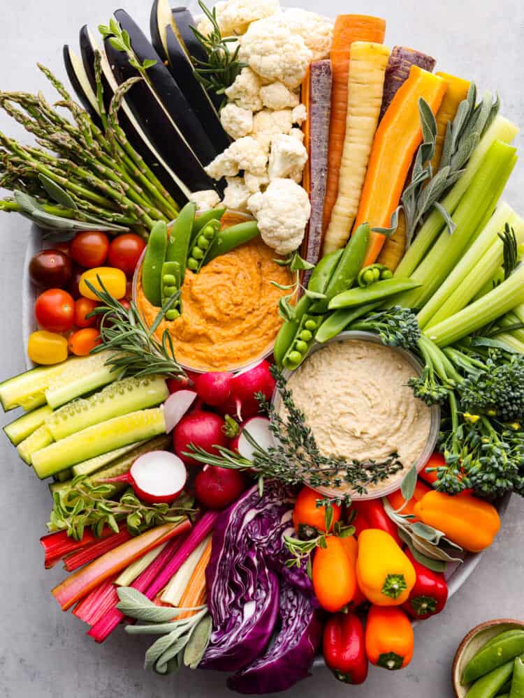 Cruditès is a French dish that is a fresh vegetable board served with delicious dips like hummus. It's the perfect way to add color and variety to your appetizers, and will be the star of your next party! A crudités tray full of vegetables and hummus.