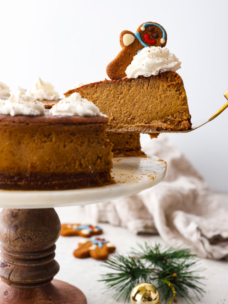 Creamy Gingerbread Cheesecake with a graham cracker crust is the perfect holiday dessert! Full of gingerbread spices and rich molasses flavor, it is sure to be your new favorite Christmas dessert! A gingerbread cheesecake on a stand with a scoop being taken out of it.