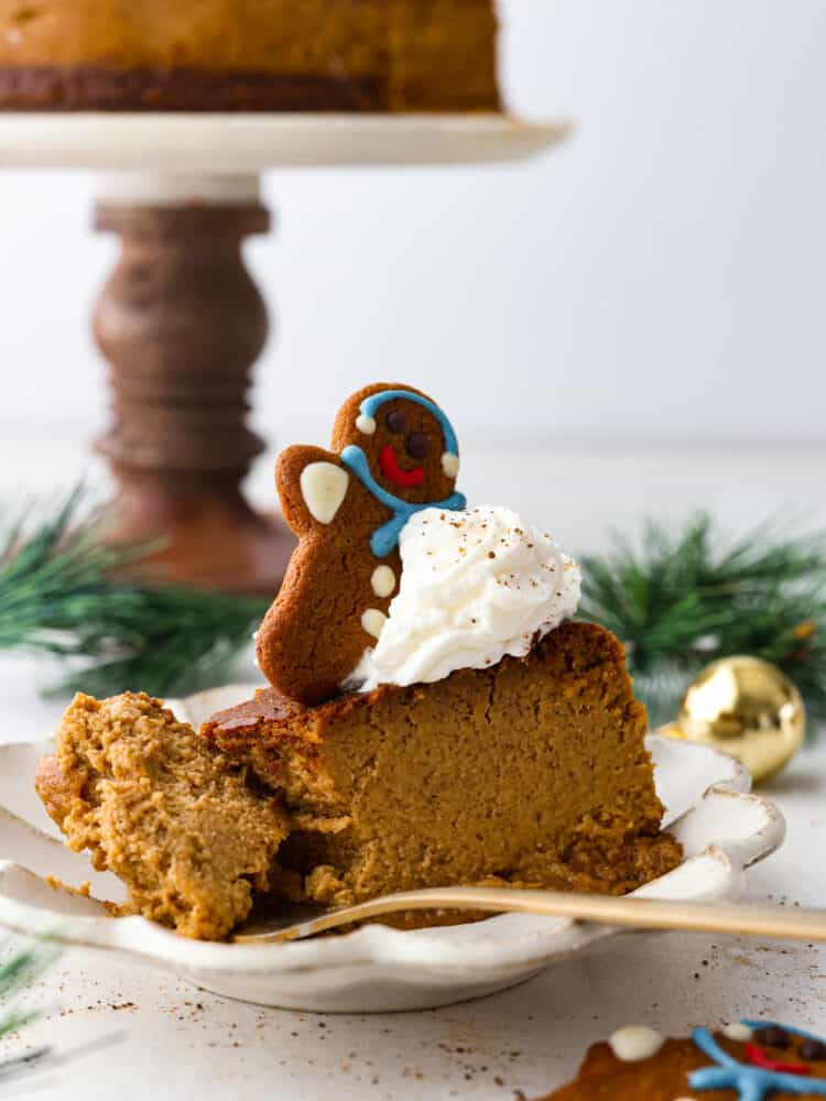 Creamy Gingerbread Cheesecake with a graham cracker crust is the perfect holiday dessert! Full of gingerbread spices and rich molasses flavor, it is sure to be your new favorite Christmas dessert! A slice of gingerbread cheesecake with a slice taken out of it with a cheesecake behind it.