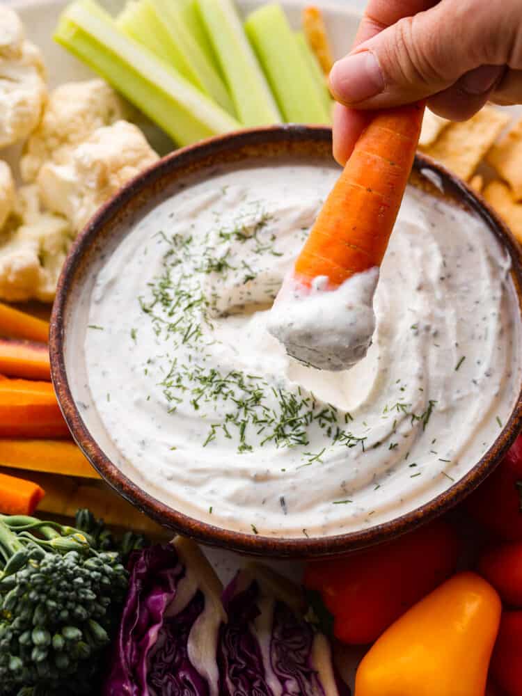 Creamy, tangy, and packed with fresh herbs, this Greek yogurt dip is the best addition to any veggie platter! Serve it up with fresh vegetables and your favorite crackers for a snack that's both healthy and delicious. A carrot being dipped into the Greek yogurt dip.