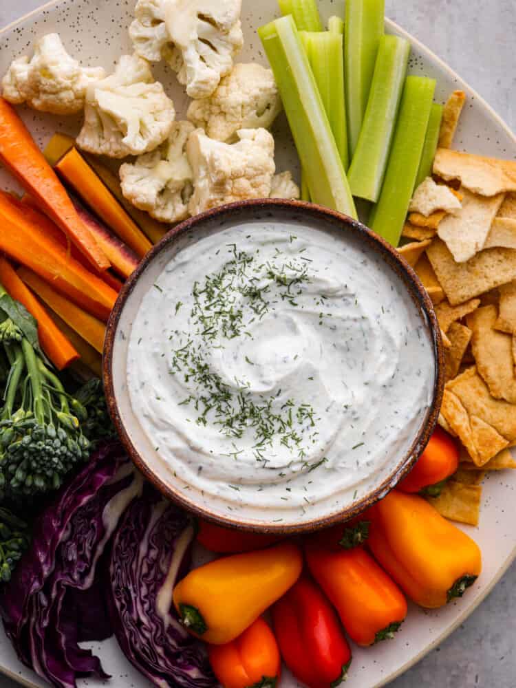 Creamy, tangy, and packed with fresh herbs, this Greek yogurt dip is the best addition to any veggie platter! Serve it up with fresh vegetables and your favorite crackers for a snack that's both healthy and delicious. Top-down view of Greek yogurt dip served with baked crackers and fresh veggies.