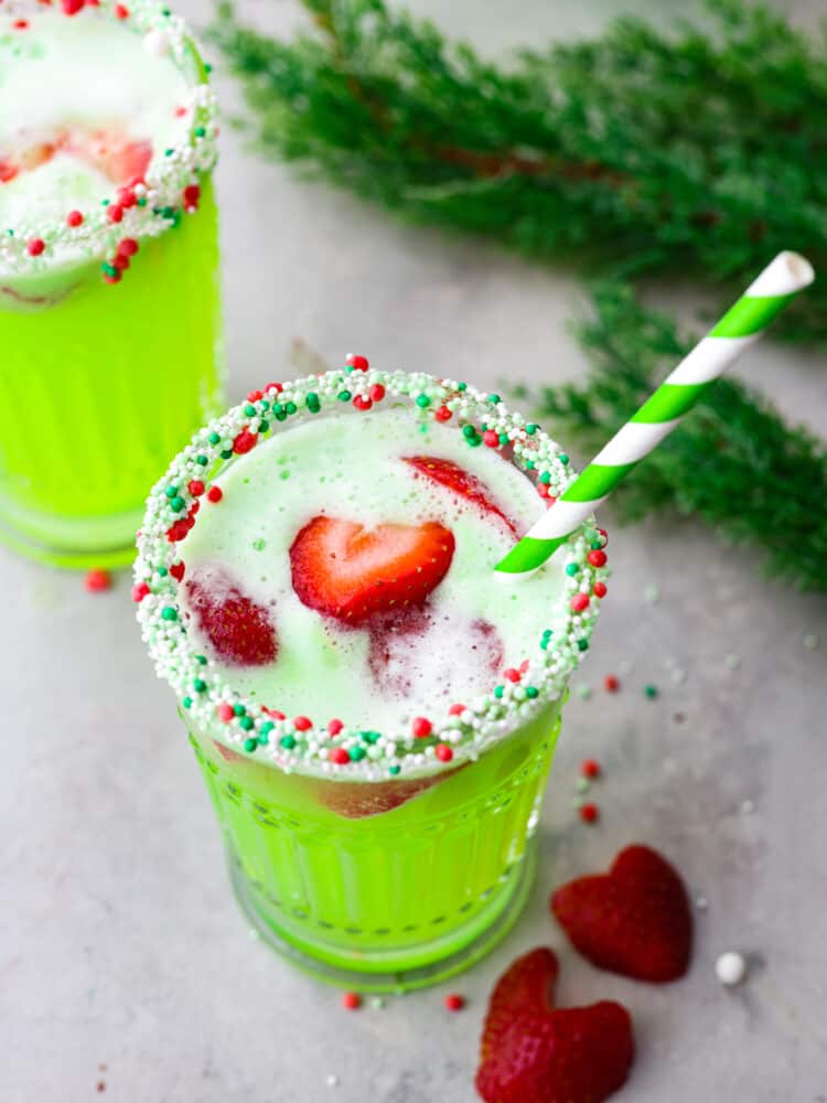 Grinch punch is a fun and festive drink for the holidays that comes together with just 4 ingredients! This tasty drink is bursting with lime and strawberry flavor. It's the perfect addition to any Christmas meal! Top-down view of Grinch punch served in a glass, garnished with strawberries and sprinkles around the rim. There is a green and white swirled straw in the glass.