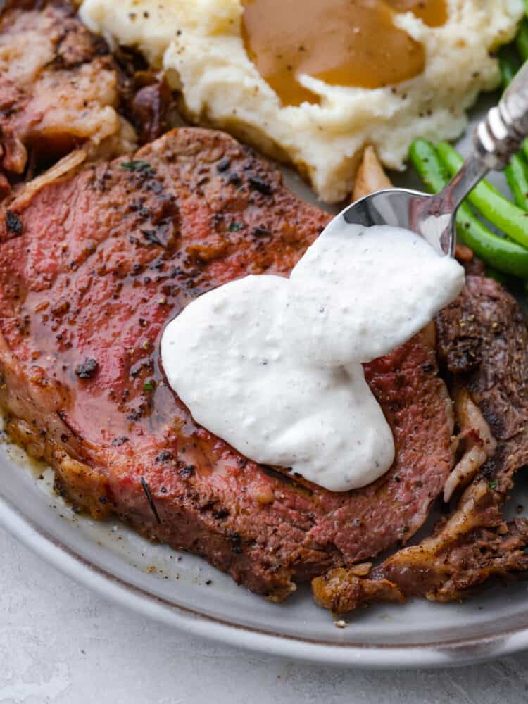 This Horseradish Sauce is creamy and full of flavor. The horseradish is strong and spicy, and paired with sour cream and other unique flavors, this sauce takes any dish to the next level! Sauce being put on top of a steak.