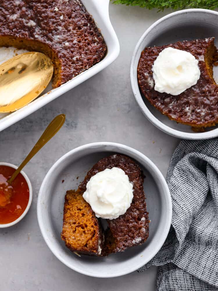 Malva pudding is a delicious cake-like dessert with an amazing caramelized outer layer. Itโs extra moist, soft, and bursting with apricot flavor. Top-down view of malva pudding served in 2 white bowls with a dollop of whipped cream on top.