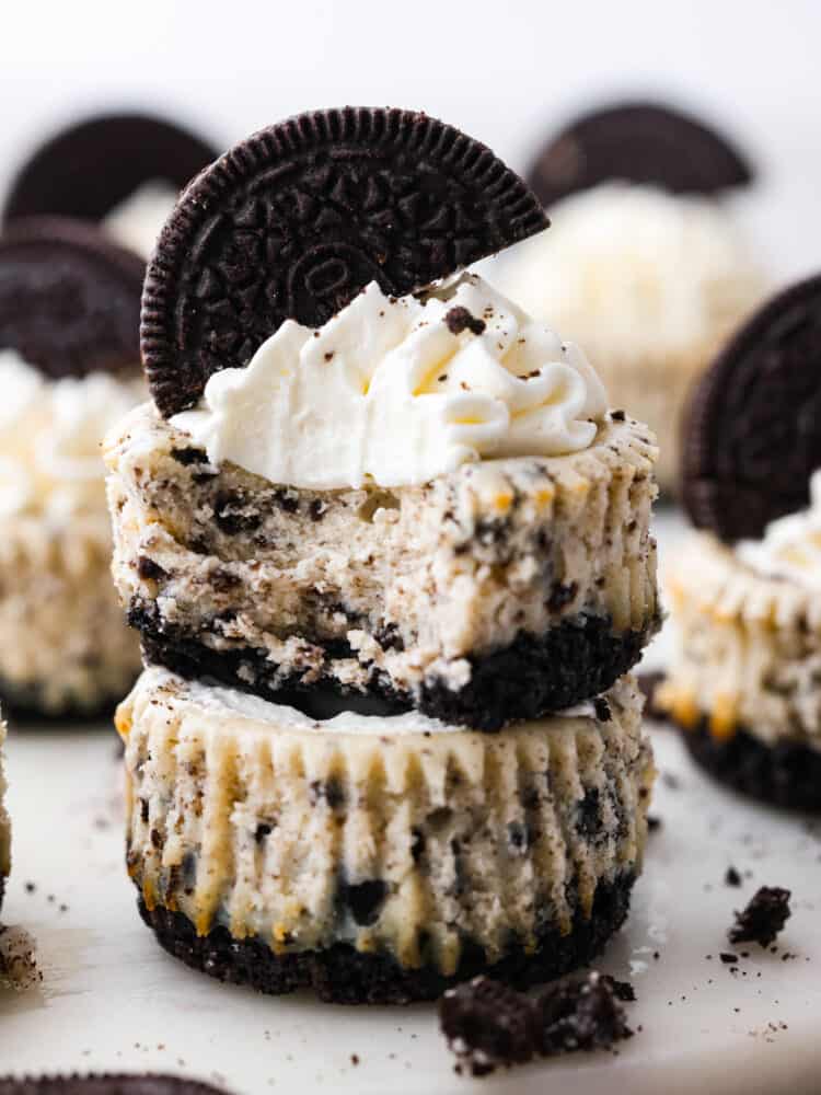 These adorable mini Oreo cheesecakes are melt-in-your mouth creamy and full of chocolate cookie flavor! Not only are they insanely good, but super easy to make as well! Be prepared for them to fly off the table in all of their smooth, chocolatey goodness. 2 cheesecake bites stacked on top of each other. One has a bite taken out of it.