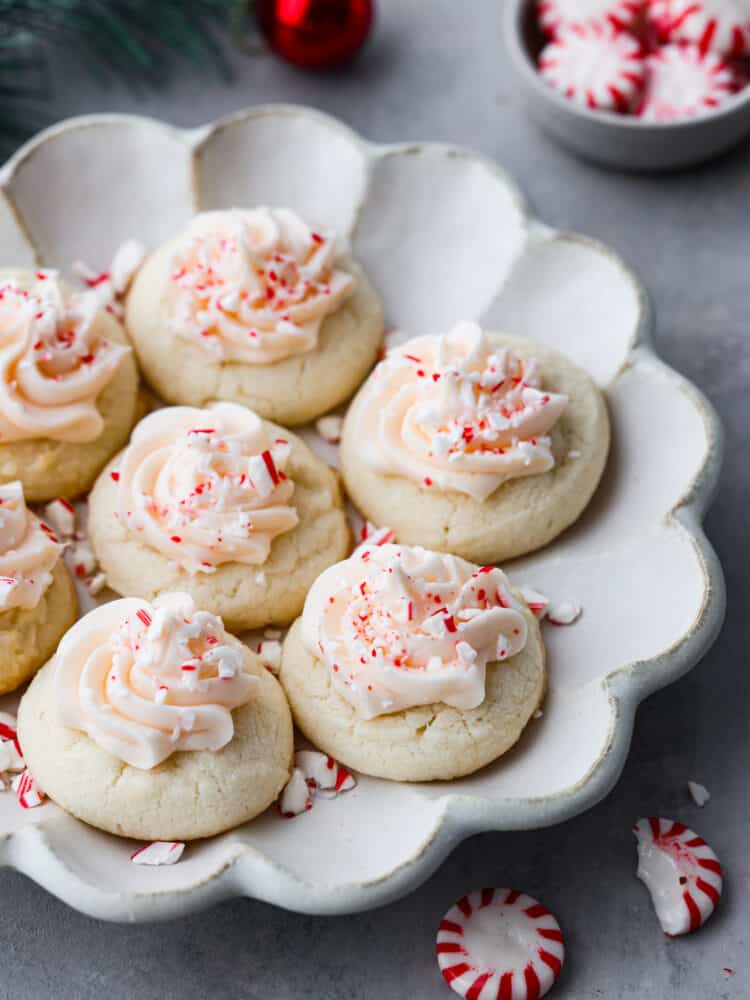These peppermint meltaways literally melt in your mouth with each and every bite. The combination of butter, powdered sugar, and cornstarch creates a fluffy and delicious cookie that everyone will LOVE! Peppermint beltways on a scalloped gray plate. Peppermint candies and ornaments surround the plate.