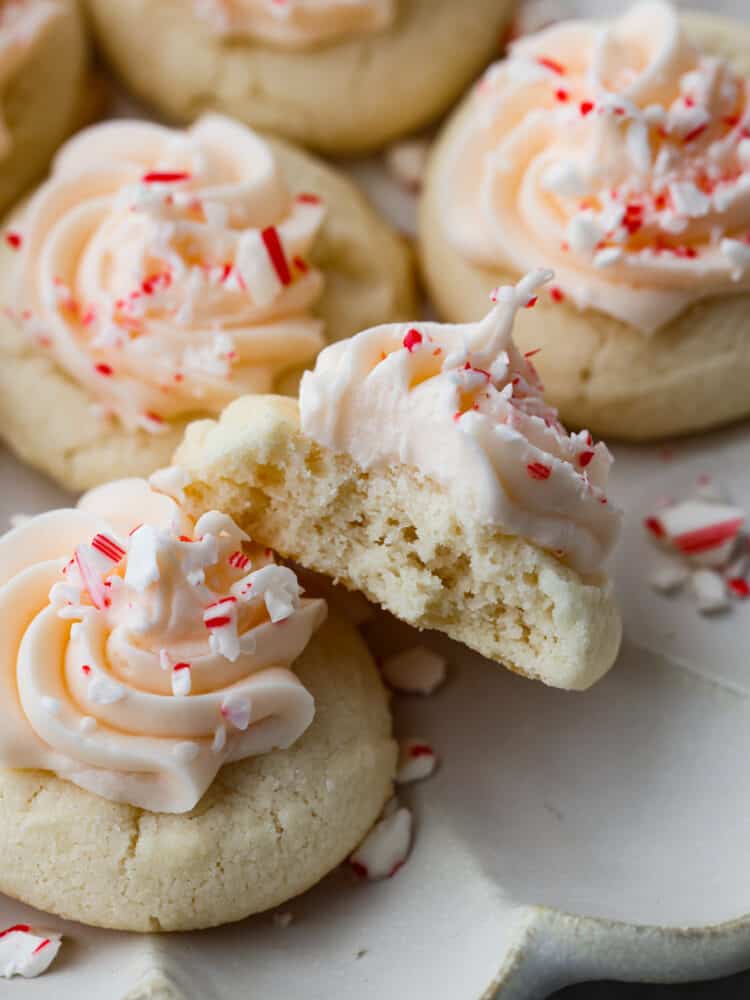 These peppermint meltaways literally melt in your mouth with each and every bite. The combination of butter, powdered sugar, and cornstarch creates a fluffy and delicious cookie that everyone will LOVE! Close up view of peppermint meltaways with frosting and sprinkled peppermint candy on top. A bite is taken out of one of the cookies