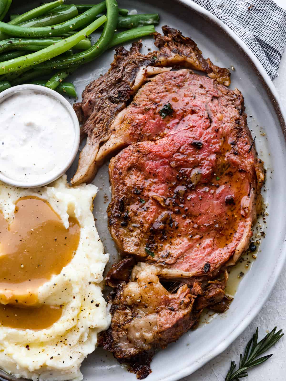 I have the perfect fool proof prime rib recipe for you. I have done all of the testing for you so that you can achieve the perfect prime rib every single time. Melt in your mouth, cooked perfectly to medium rare with a perfect garlic butter crust, this recipe is incredible. I will help you feel confident every step of the way! Plated slice of prime rib next to a horseradish cup, green beans, and mashed potatoes and gravy.