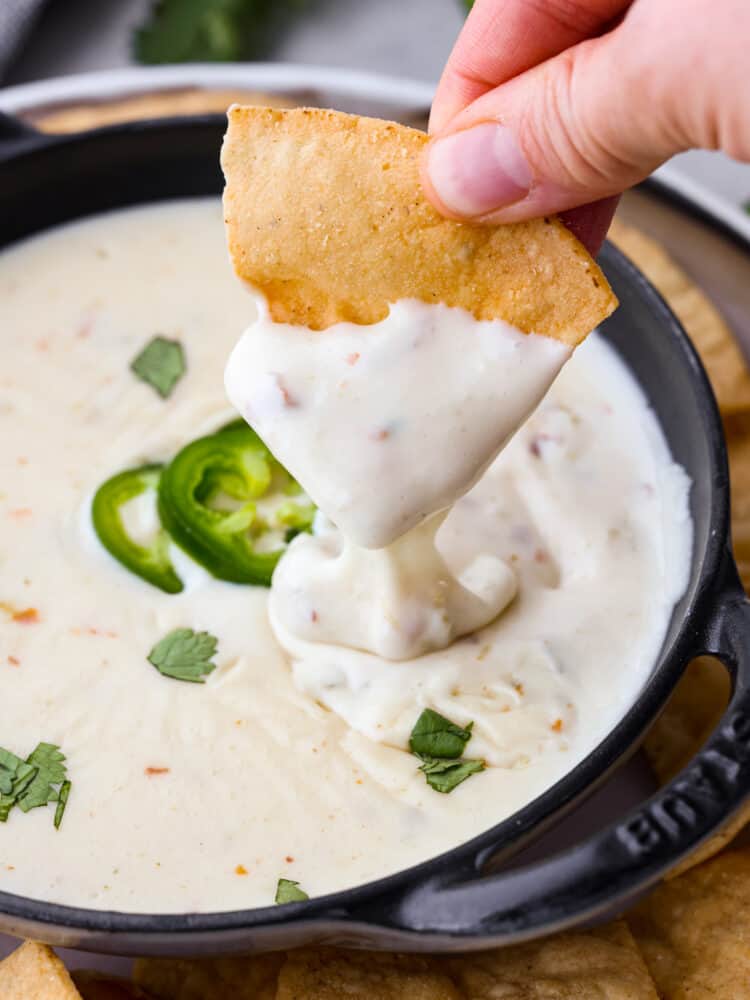 My Queso Blanco is creamy, dreamy, and seriously so addictive. The secret? White American cheese! It melts like a dream, gives you that ultra-smooth texture! A tortilla chip being dipped into queso blanco.