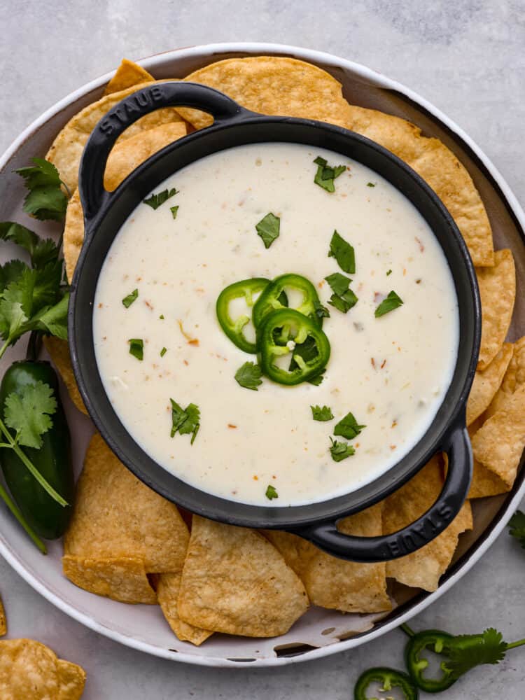 My Queso Blanco is creamy, dreamy, and seriously so addictive. The secret? White American cheese! It melts like a dream, gives you that ultra-smooth texture! Queso blanco dip in a black bowl with fresh jalapenos and chips around it.