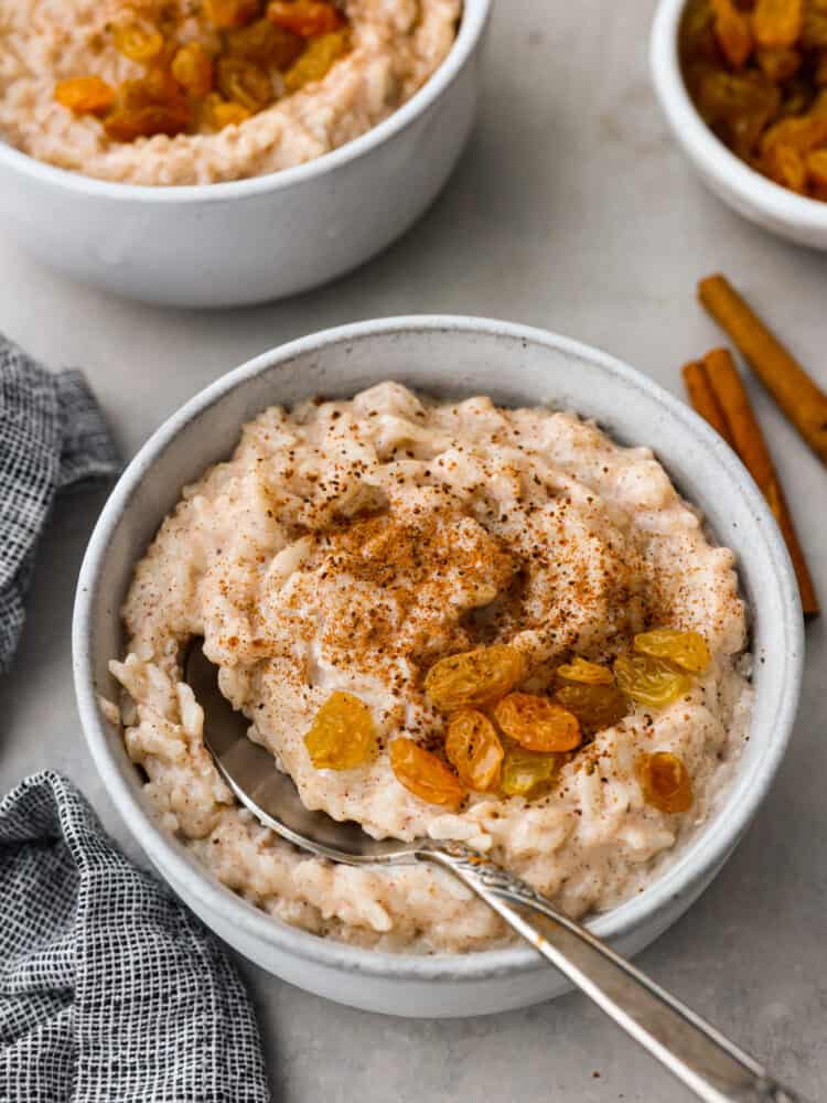 Rich, creamy rice pudding is delicious warm or cold, and lightly spiced with just a hint of cinnamon and nutmeg. It's the coziest, most comforting dessert of all! We love it with plump golden raisins! A bowl of rice pudding with a spoon in it.