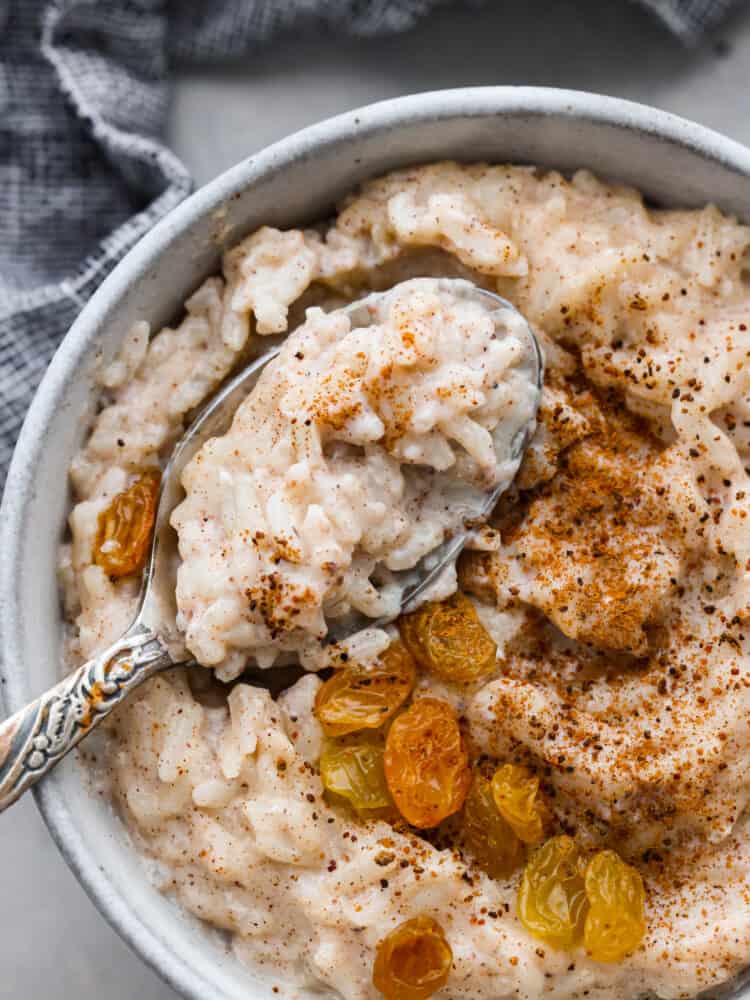 Rich, creamy rice pudding is delicious warm or cold, and lightly spiced with just a hint of cinnamon and nutmeg. It's the coziest, most comforting dessert of all! We love it with plump golden raisins! Closeup of rice pudding served with cinnamon, nutmeg, and raisins on top.