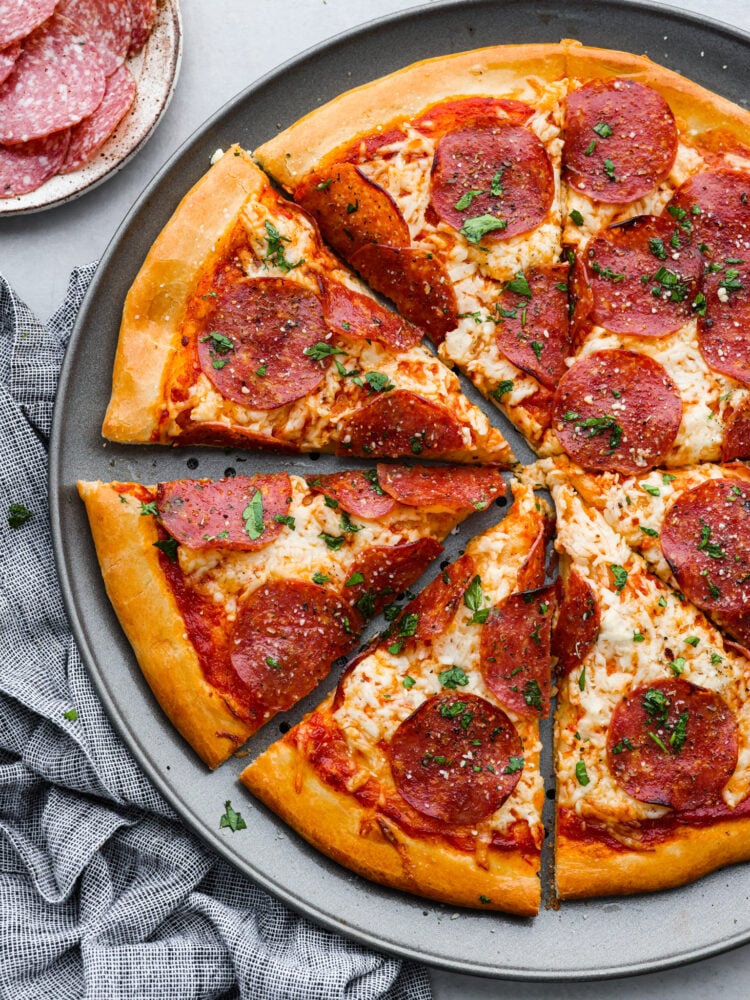 Salami Pizza is a quick and easy recipe that is sure to satisfy the whole family! A homemade pizza with all the flavor of your favorite pizzeria that is ready in just under 30 minutes, this salami pizza is definitely going to be one you come back to again and again. Salami pizza on a pizza pan cut into slices.
