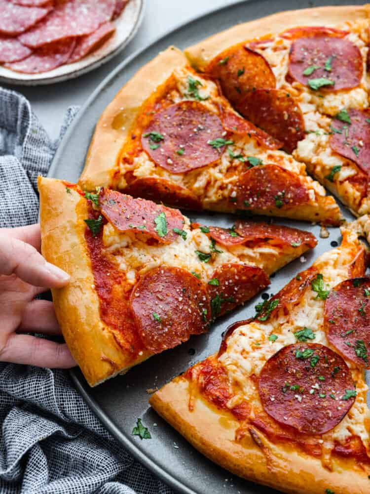 Pillowy soft, with the perfect taste and texture, this quick and easy pizza dough is going to be your go-to recipe for everything! You are going to want to keep this in the archives and use it over and over again. A slice of pepperoni pizza being picked up.