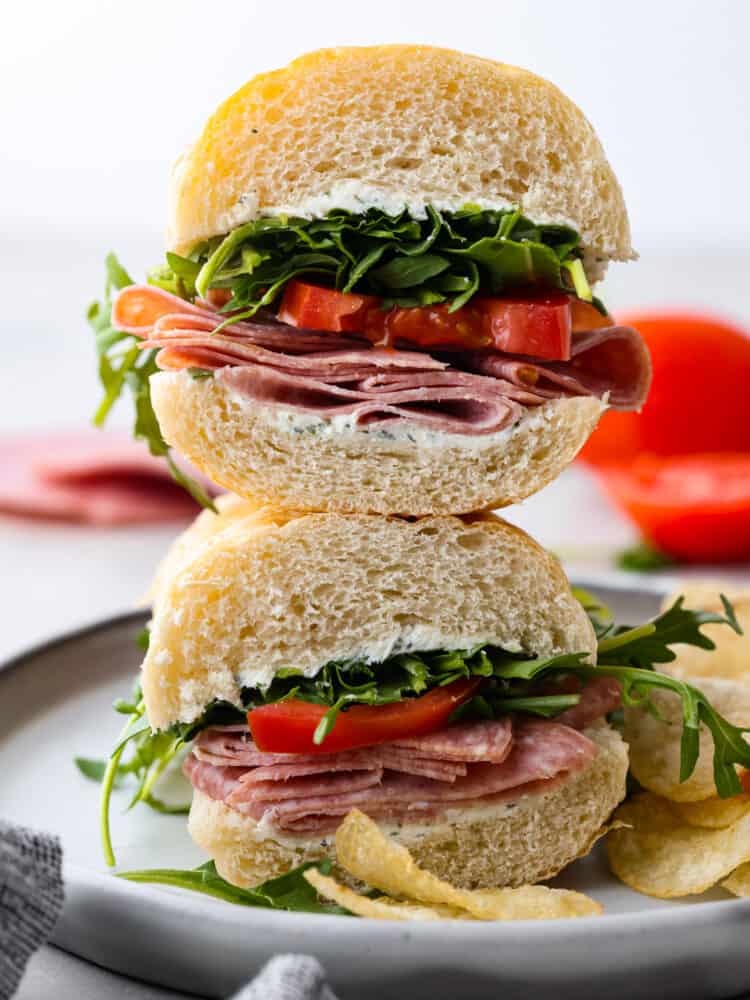 This simple and refreshing Salami Sandwich is full of salami, garlic and herb cream cheese, tomato and arugula. It's a flavor packed and quick meal that is sure to satisfy! A salami sandwich cut in half and stacked on top of each other.