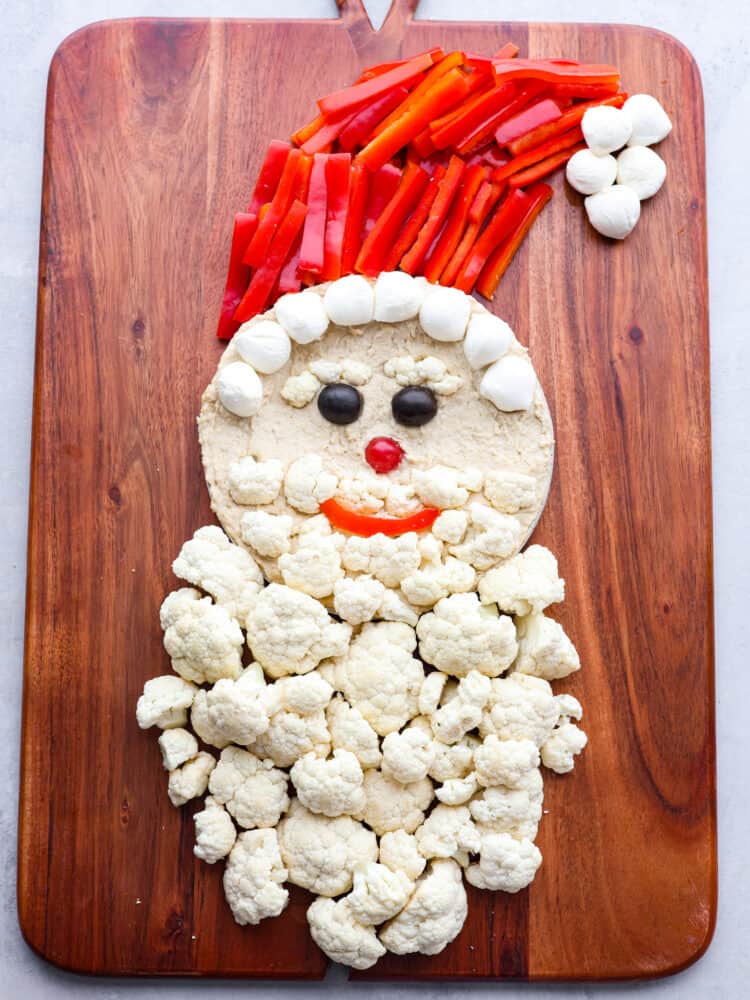 Skip the store-bought platters and make this Santa veggie tray instead! It's a healthy and delicious way to add a little extra holiday cheer to all of your Christmas get-togethers. Santa's beard being made out of cauliflower florets.