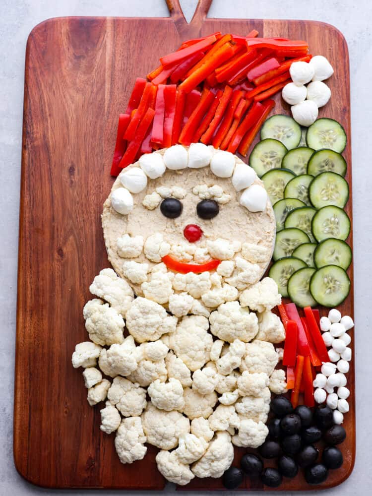 Skip the store-bought platters and make this Santa veggie tray instead! It's a healthy and delicious way to add a little extra holiday cheer to all of your Christmas get-togethers. Santa's arms being made out of sliced red peppers and olives.