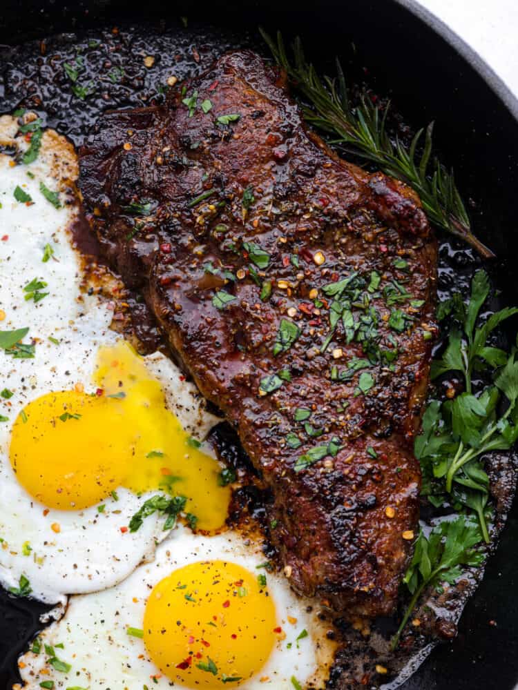Steak and eggs is a hearty and delicious breakfast packed with protein and flavor! Tender and juicy pan-seared steak is seasoned to perfection and served alongside eggs sunny side up. Close view of steak and eggs in a black skillet and garnished with fresh parsley.