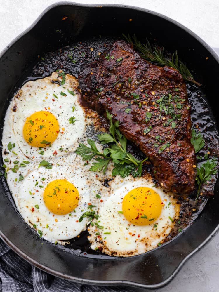Steak and eggs is a hearty and delicious breakfast packed with protein and flavor! Tender and juicy pan-seared steak is seasoned to perfection and served alongside eggs sunny side up. Top view of steak and eggs in a black skillet and garnished with fresh parsley.