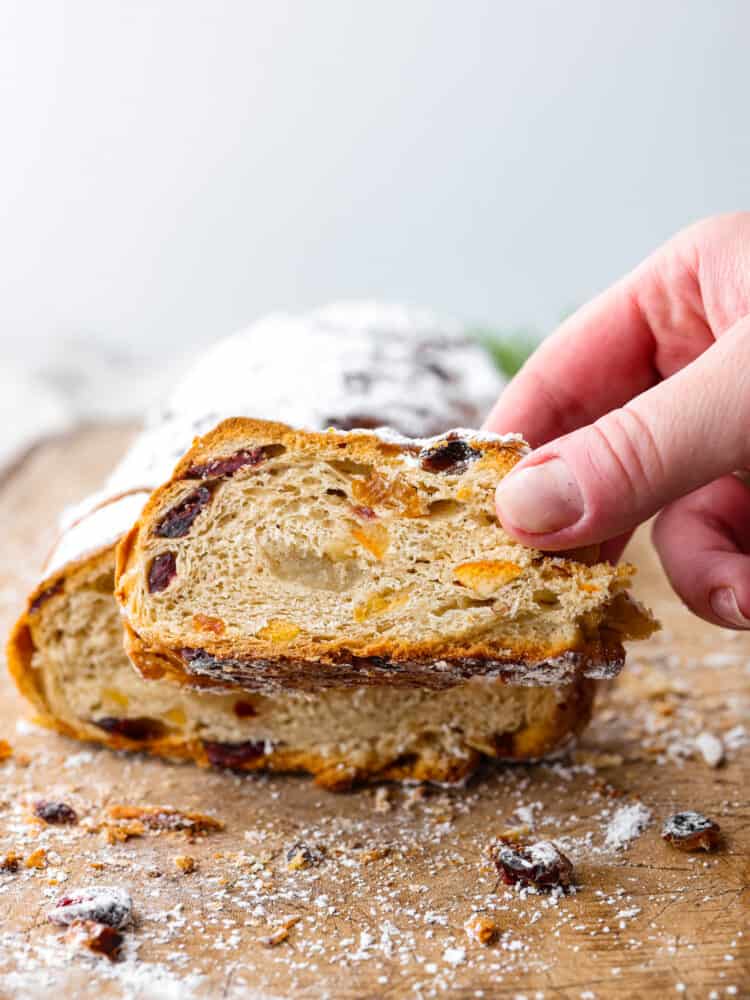 This traditional German stollen bread is the perfect treat for the holidays! It's a delicious sweet bread filled with cranberries, raisins, candied citrus, and a luscious almond filling. Front view of stollen with a slice being picked up.