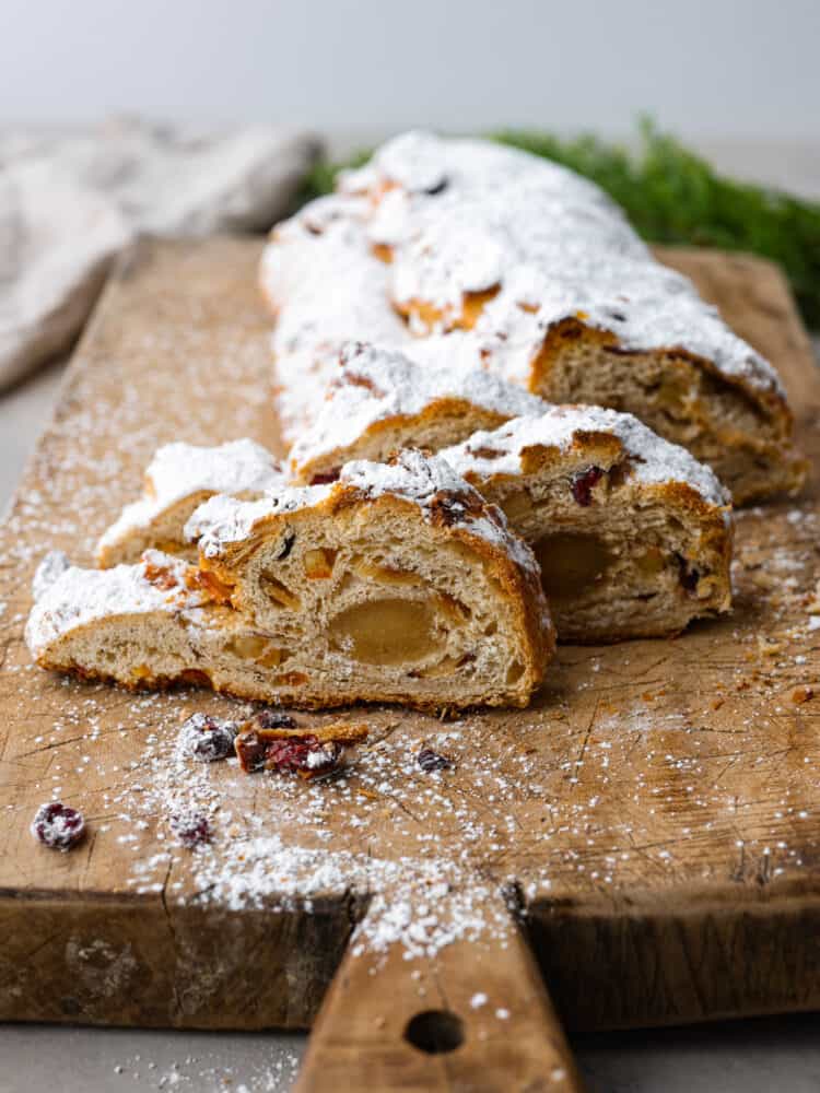 This traditional German stollen bread is the perfect treat for the holidays! It's a delicious sweet bread filled with cranberries, raisins, candied citrus, and a luscious almond filling. Hero image of sliced stollen bread on a wooden board.