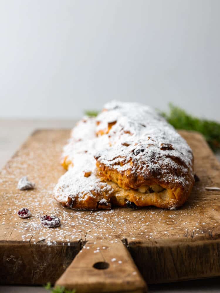 This traditional German stollen bread is the perfect treat for the holidays! It's a delicious sweet bread filled with cranberries, raisins, candied citrus, and a luscious almond filling. A loaf of stollen on a wooden board.