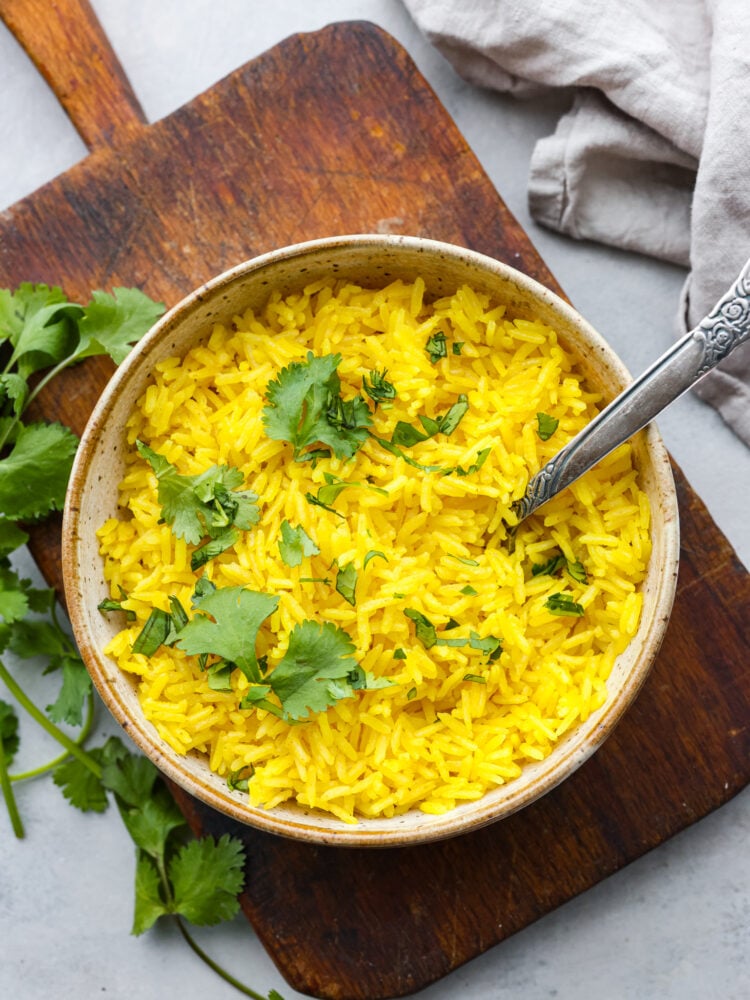 Ready in 20 minutes, this yellow rice is quick and easy and packed with savory flavor! It's the perfect side dish for busy weeknight dinners. Top-down view of yellow rice in a stoneware bowl, served on top of a wooden board.