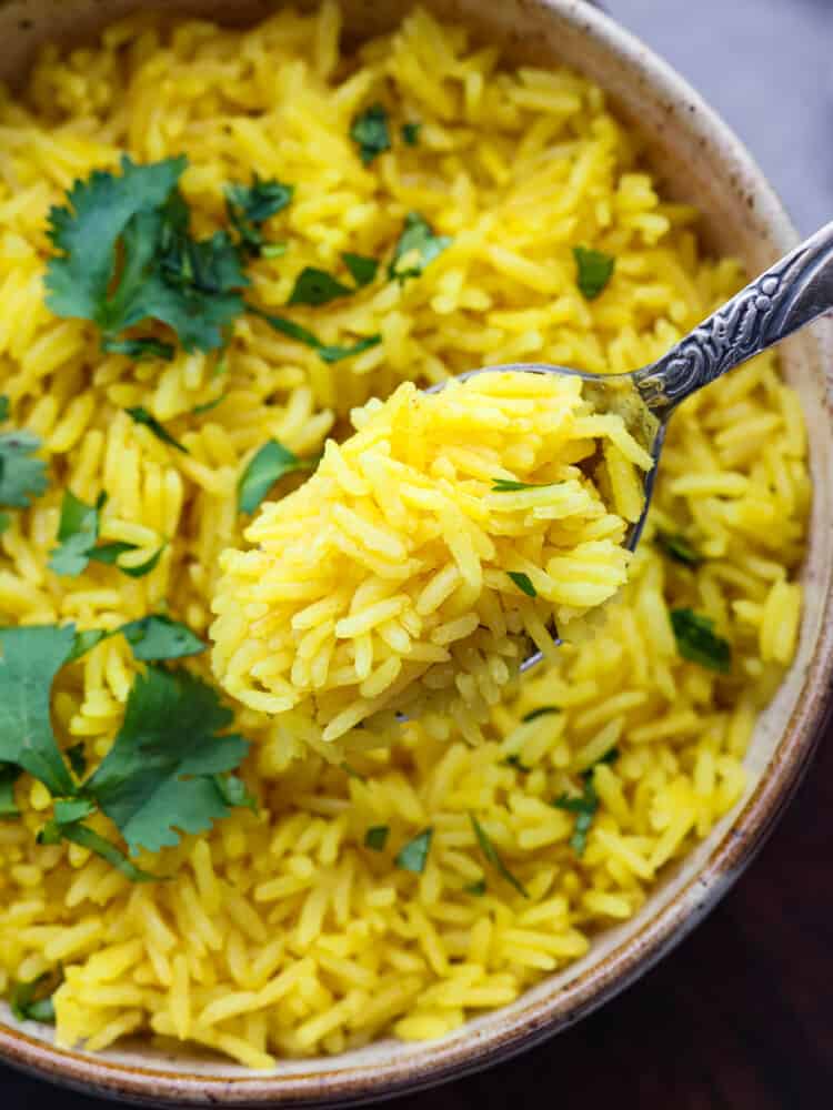Ready in 20 minutes, this yellow rice is quick and easy and packed with savory flavor! It's the perfect side dish for busy weeknight dinners. Closeup of yellow rice on a metal spoon.