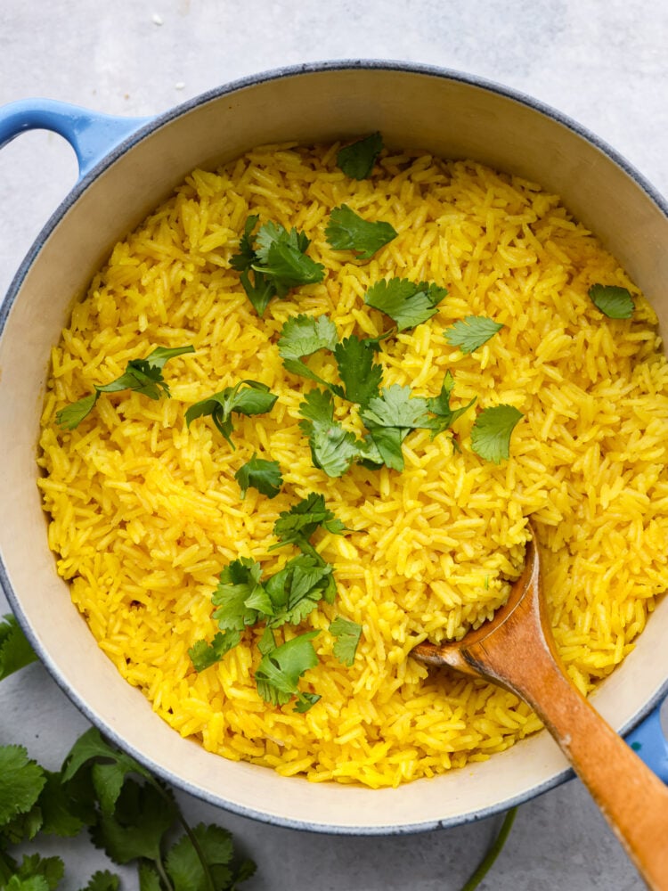 Ready in 20 minutes, this yellow rice is quick and easy and packed with savory flavor! It's the perfect side dish for busy weeknight dinners. Top-down view of yellow rice in a white and blue skillet, garnished with cilantro.