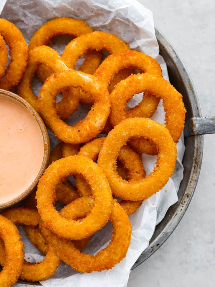 You are going to love how crispy and perfectly cooked these Air Fryer Frozen Onion Rings get! They are so simple, and you can have frozen onion rings cooked to crispy perfection in minutes. You'll love serving them along with a burger or as an appetizer at your next gathering. Air fryer frozen onion rings on a plate with parchment paper.
