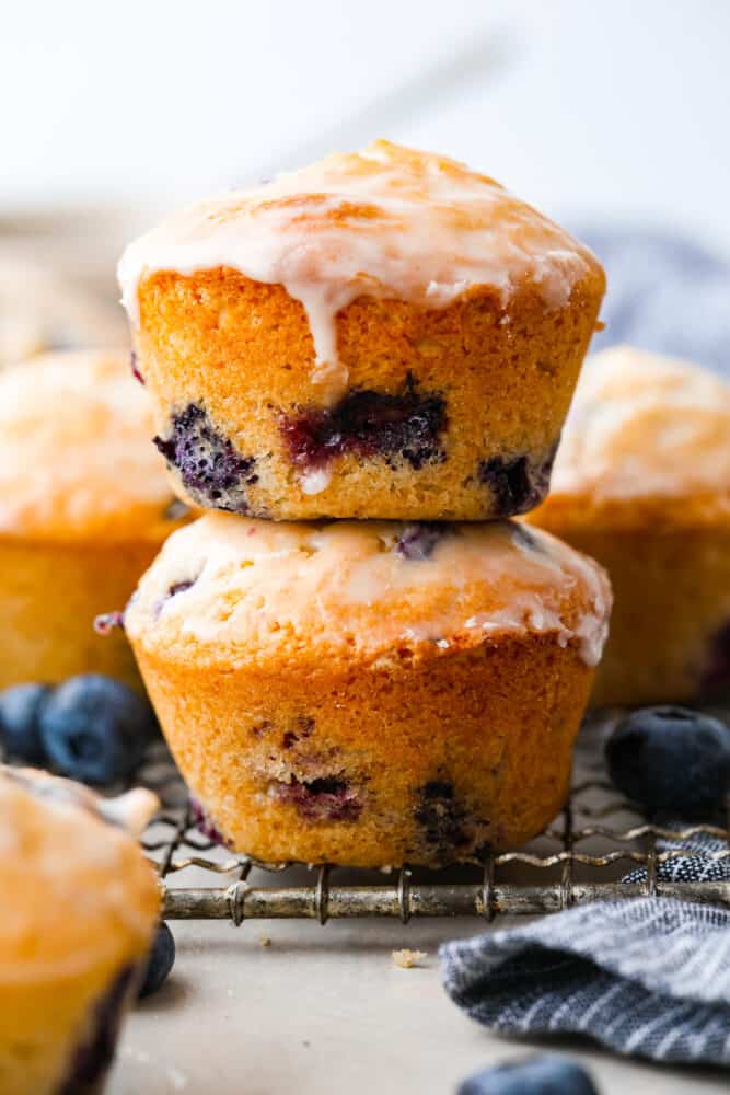 These blueberry muffins with a sugared glaze are so good, they should be illegal! Soft, buttery, and bursting with sweet blueberry flavor, they're the perfect excuse to have dessert for breakfast. 2 muffins stacked on top of each other.