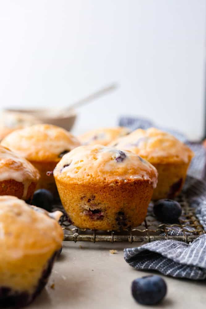 These blueberry muffins with a sugared glaze are so good, they should be illegal! Soft, buttery, and bursting with sweet blueberry flavor, they're the perfect excuse to have dessert for breakfast. Hero image of blueberry muffins on a wire rack.
