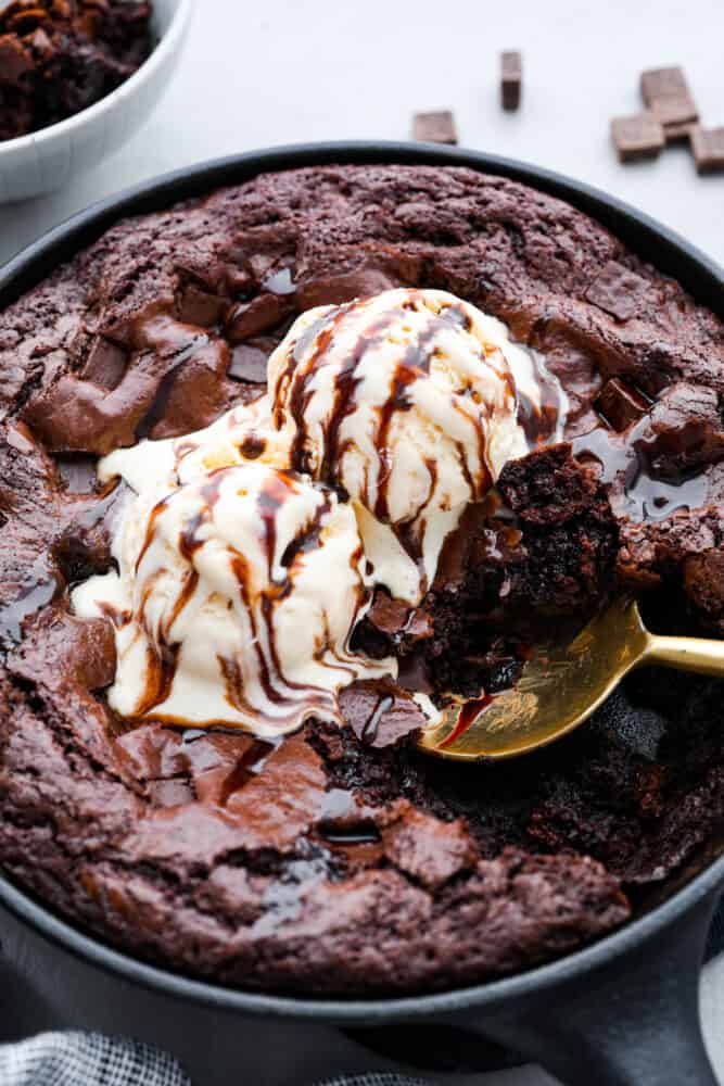 This easy skillet brownie is just the chocolatey, ooey-gooey dessert you need in your life! Top it off with a scoop of vanilla ice cream for the ultimate indulgent treat you can enjoy straight from the pan! Hero image of a skillet brownie topped with ice cream and chocolate sauce.