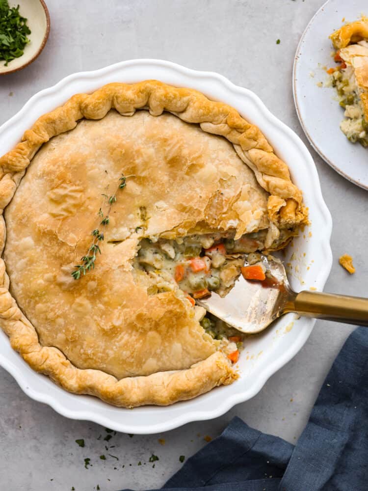 There is nothing more comforting than this absolutely perfect chicken pot pie! A flaky pie crust filled with chicken, veggies, and tons of flavor is just what you need on a cold winter day, or any day. This is a classic recipe you will definitely want in your recipe book! Beautiful chicken pot ipe with a slice taken out of it in a white pie dish.